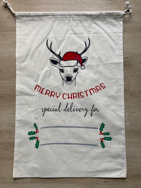 Natural canvas Christmas gift sack with postal theme, featuring gold 'NORTH POLE EXPRESS' heading, black Santa sleigh silhouette, red North Pole official stamp, 'SPECIAL DELIVERY' gold text, personalized delivery address space, and 'IF UNDELIVERED RETURN TO SANTA CLAUS NORTHPOLE' footer, drawstring canvas bag resembling official Santa mail by AJ's Infinity Design