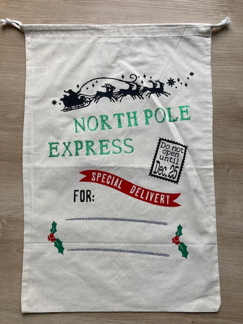 Natural canvas Christmas gift sack with 'NORTH POLE EXPRESS' custom print in green, featuring flying Santa sleigh silhouette, 'SPECIAL DELIVERY' red banner, 'Do not open until Dec 25' stamp, and personalization space with holly accents, drawstring canvas bag for personalized holiday gifts by AJ's Infinity Design
